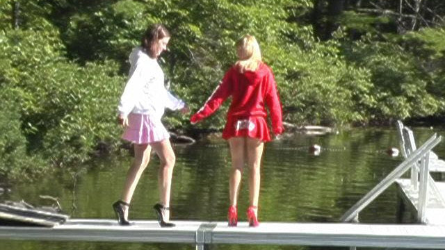 Two people on a dock by a lake with trees in the background