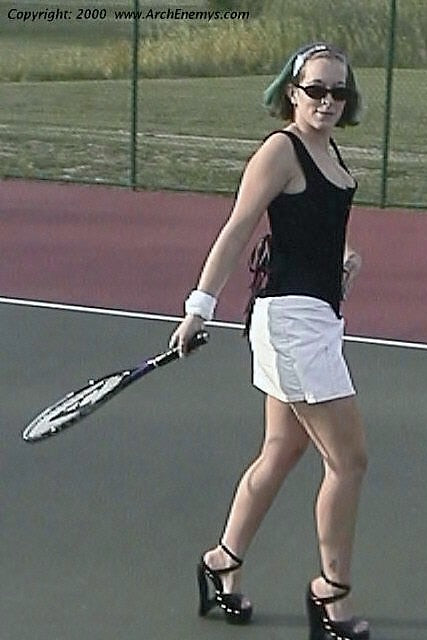 Woman on a tennis court holding a racket, wearing a black top and white shorts.