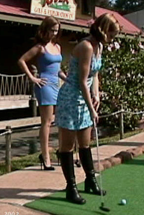 Two women playing mini golf at a themed course with tiki decorations.