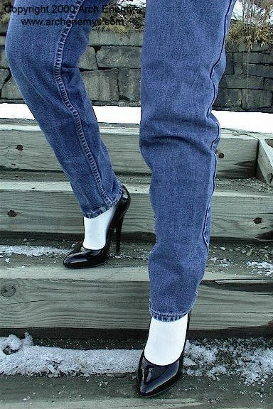 Person wearing blue jeans and black high heels on a snowy ground.
