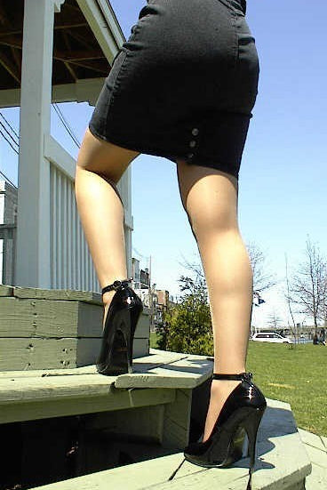 Person wearing a black skirt and high heels on a wooden platform with a clear blue sky.