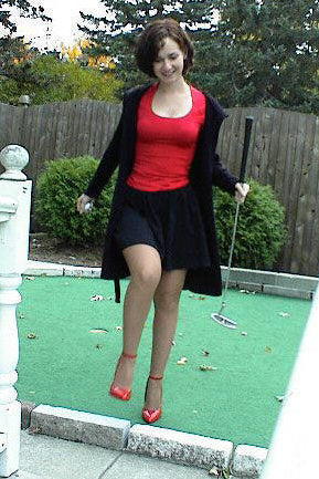 Woman playing mini golf on a green course with trees and a wooden fence in the background.