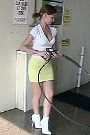 Woman in a white top and yellow skirt using a car wash hose in a garage.