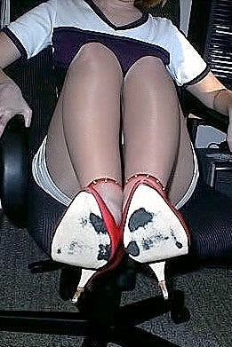Randi Johnson wearing pantyhose and high heels sitting in an office chair in a room with office furniture.