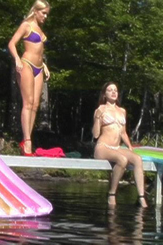 Two women in bikinis by a pool with an inflatable slide and colorful pool toys.