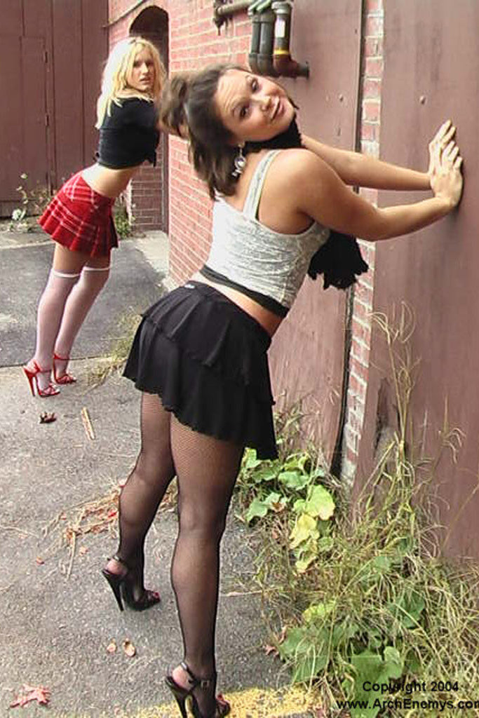 Two women in casual outfits standing against a brick wall.