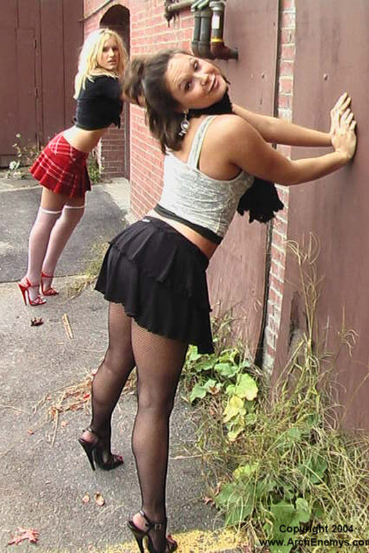 Two women in casual outfits standing against a brick wall.