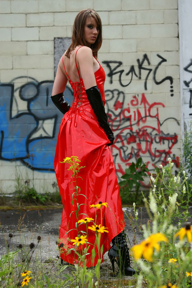 Woman in a red dress standing amidst wildflowers with graffiti on the wall behind her