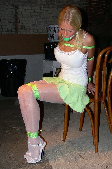 Person in a white dress with green tape sitting on a chair in a dimly lit room.