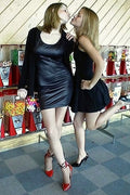 Two women in black dresses standing next to a snack cart with colorful treats.