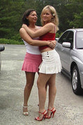Two women hugging in a parking lot with cars and trees in the background.