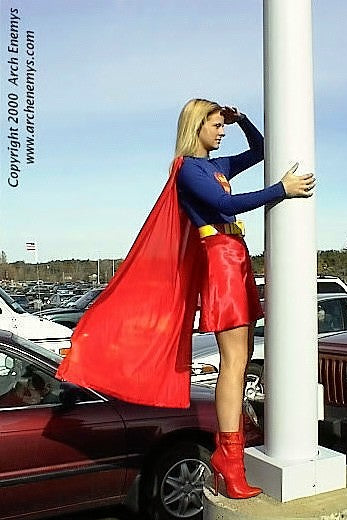 Person in a Superman costume standing next to a pole in a parking lot.