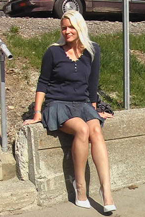 Woman sitting on a concrete ledge by a set of stairs with a car in the background.