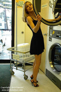 Woman in a black dress standing next to a washing machine in a laundromat.
