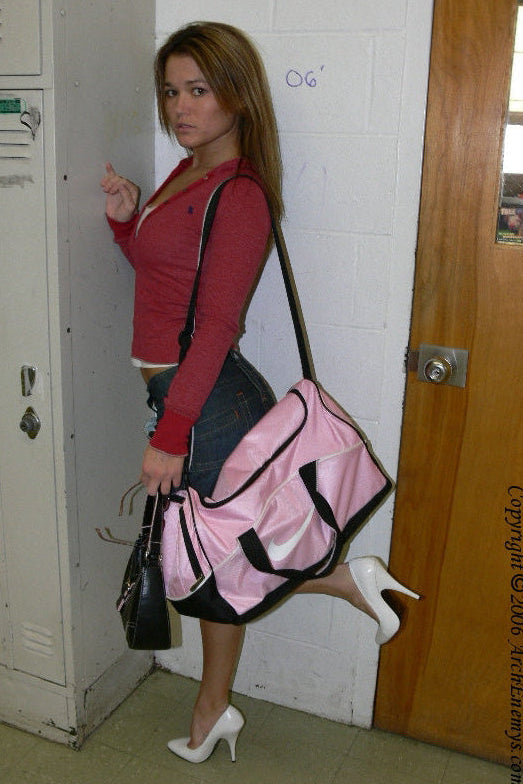 Woman in a red sweater and black skirt standing next to a locker with a pink and black bag.