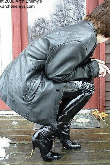 Person in a gray leather jacket and black high-heeled boots on a wooden porch with snow and bare trees in the background.