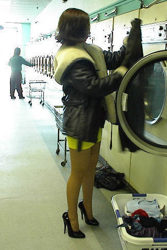 Person in a laundromat with a washing machine and clothes.