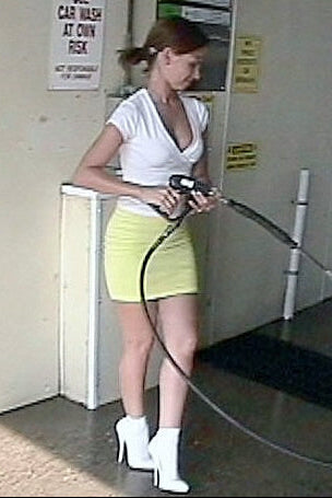Woman in a white top and yellow skirt using a car wash hose in a garage.